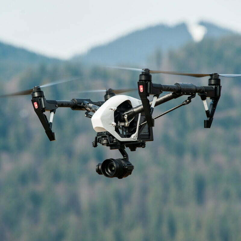 White drone with digital camera flying in sky over mountain